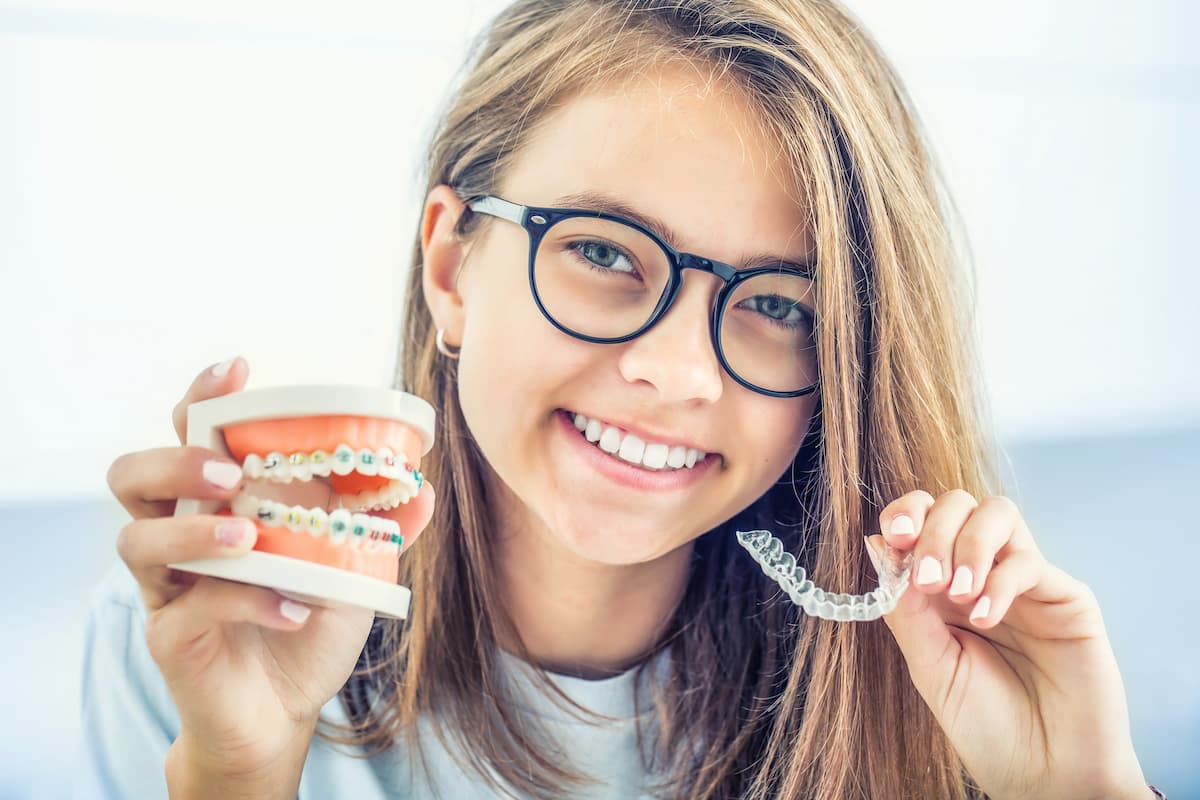 Jeune qui souriante qui tiens un appareil orthodontique invisible et un traditionnel